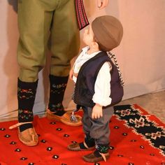 a little boy standing on top of a red rug next to a man in green pants