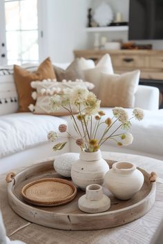 a tray with vases and flowers sitting on top of a white couch in a living room