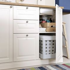 a kitchen with white cupboards and drawers filled with items on the counter top, next to a multicolored rug