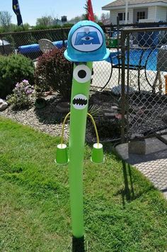 a green and blue pole with eyes on it in the grass next to a fence