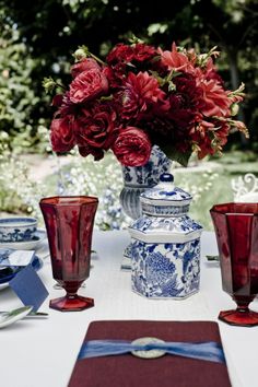 red flowers are in a vase on a table with blue and white dishes, napkins, and place settings