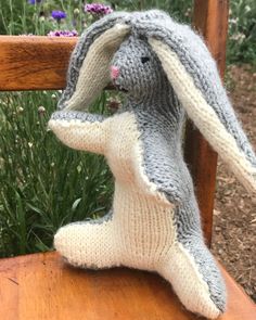 a knitted bunny sitting on top of a wooden chair next to purple and white flowers