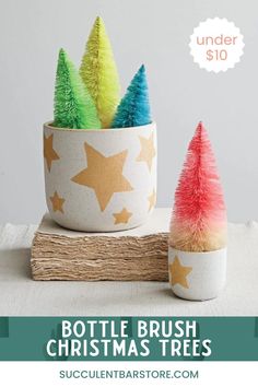 two small christmas trees are in a white cup with gold stars on it and the words, bottle brush christmas trees