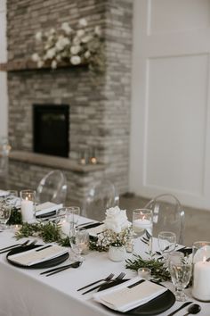 the table is set with white flowers and candles for an elegant wedding reception in front of a fireplace