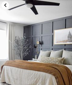 a bedroom with gray paneling, white bedding and a brown blanket on the headboard