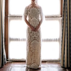 a woman standing in front of a window with her hands on her hips wearing a white dress