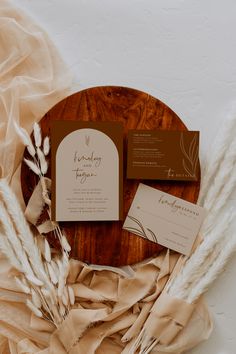 the wedding stationery is laid out on a wooden plate with some dried flowers and feathers