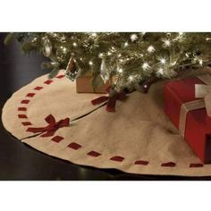 a christmas tree with presents under it on a rug in front of a lit christmas tree