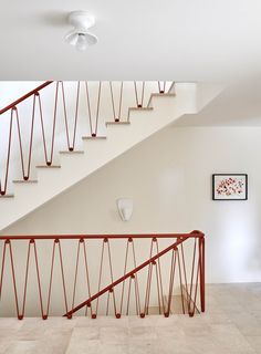 a white staircase with red handrails next to a framed painting on the wall