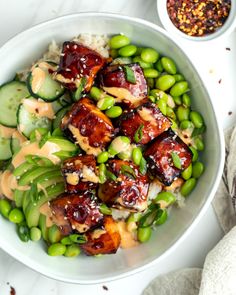 a white bowl filled with meat and vegetables next to a small bowl of sauce on the side