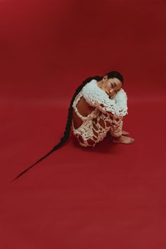 a woman sitting on the ground with her arms around her body and wearing a white crochet dress