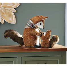 a stuffed animal squirrel on top of a wooden table next to a wall with flowers