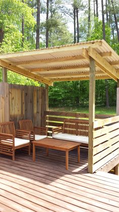 a wooden deck with benches and tables under a pergolated roof over looking a wooded area