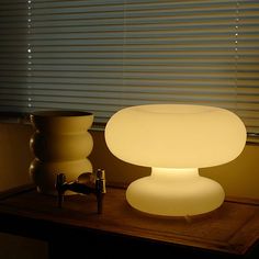 a table lamp sitting on top of a wooden table next to a vase and cup