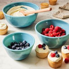 cupcakes and berries in blue bowls on a marble counter with other dessert items