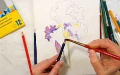 someone is drawing with colored pencils on paper