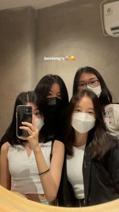 three women wearing face masks are taking a selfie in the mirror with their cell phone