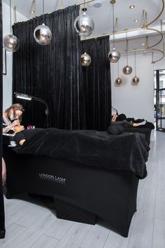 two women laying on a bed in a room with black drapes and lights hanging from the ceiling