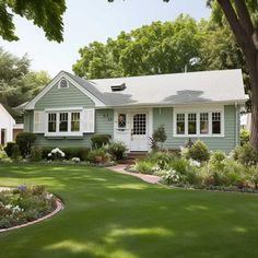 a green house with white shutters and trees in the front yard on a sunny day