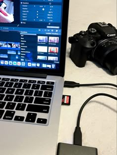 an open laptop computer sitting on top of a white table next to a camera and other electronics