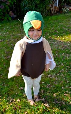 a little boy dressed up as a bird in the grass with leaves on it's head