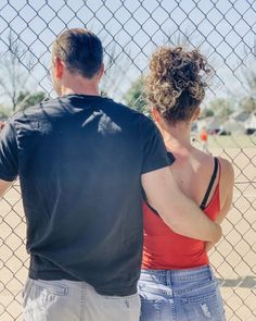 a man and woman standing next to a fence