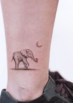 an elephant tattoo on the ankle with a crescent moon and red dot in its trunk