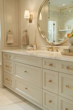 a large bathroom with white cabinets and gold accents on the countertop, along with a round mirror