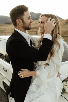 a bride and groom hugging in front of a white car