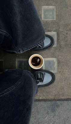 a person standing with their feet on the ground holding a cup of coffee