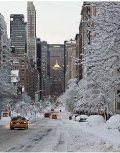 cars driving down a snow covered street in the middle of tall buildings and skyscrapers