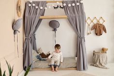 a small child sitting on top of a bed in a room with curtains and toys