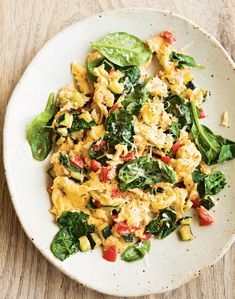 a white plate topped with eggs and spinach on top of a wooden table next to a fork