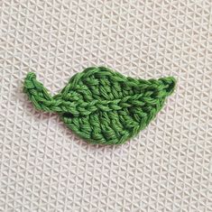 a crocheted green leaf sitting on top of a white cloth covered tablecloth