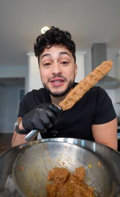 a man in black shirt holding up a large piece of bread over a metal bowl