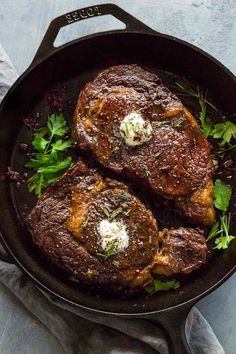 two steaks in a skillet with parsley and butter on the side, ready to be eaten