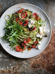 a white plate topped with pasta and veggies on top of a metal table