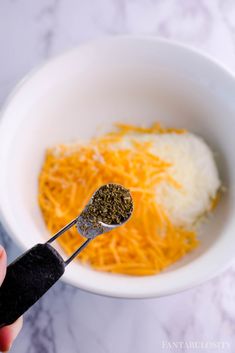 a person holding a spoon in a bowl with cheese and seasoning on the side