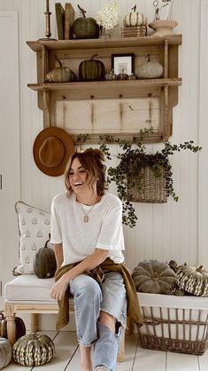 a woman sitting on top of a wooden bench next to a shelf filled with pumpkins