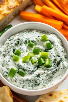 a white bowl filled with dip surrounded by carrots and pita bread