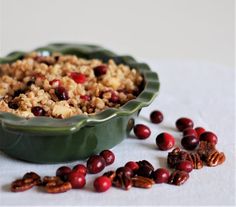 a green bowl filled with cranberries and pecans on top of a table