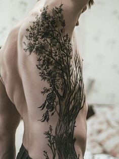 a man with a tree tattoo on his back is standing in front of a bed