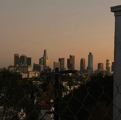 the city skyline is seen through a chain link fence at sunset in this view from across the street