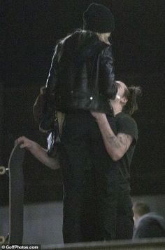 a man and woman hug while standing next to a skateboard