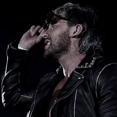 a man in black leather jacket singing into a microphone with his hand up to his face