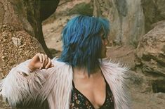 a woman with blue hair standing in front of rocks