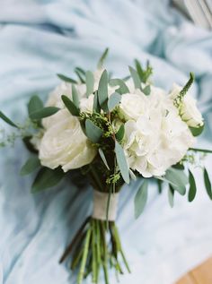 a bouquet of white flowers sitting on top of a blue cloth covered bed sheet with greenery