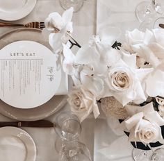 the table is set with white flowers and silverware