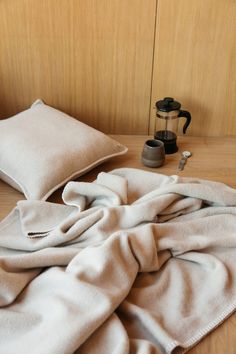 an unmade bed with two pillows and some coffee mugs on the table next to it