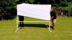 a man and woman standing in front of a white sheet on top of a green field